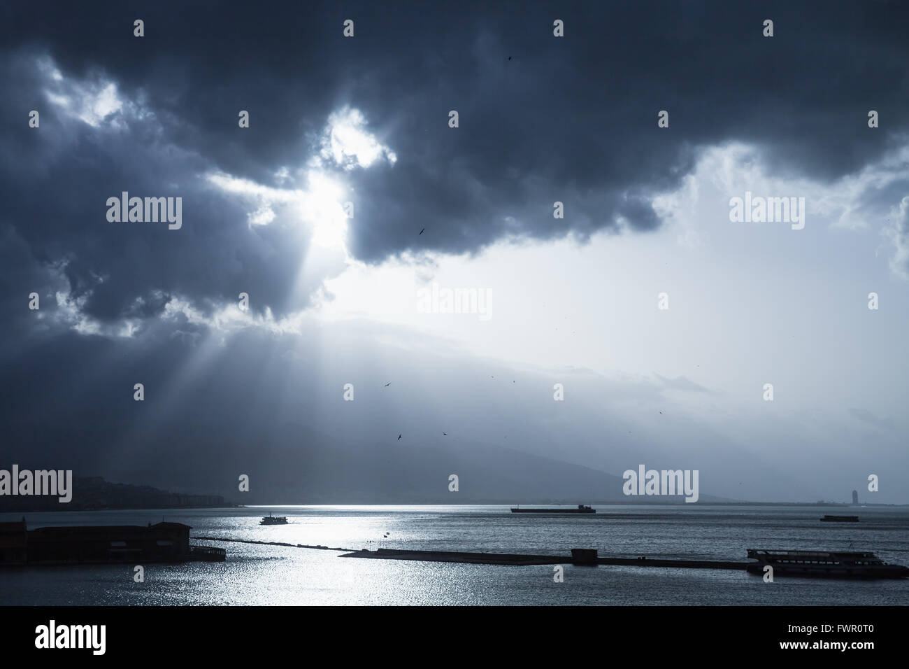 Dark dramatic sky with sunlight rays over sea. Blue toned photo filter effect Stock Photo