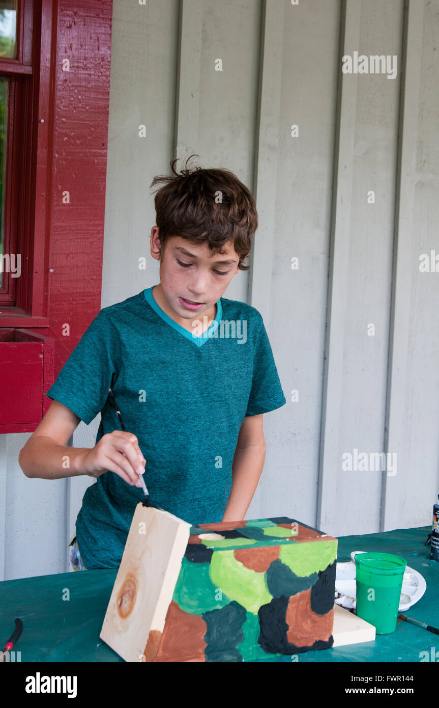 boy at camp painting a birdhouse craft project Stock Photo