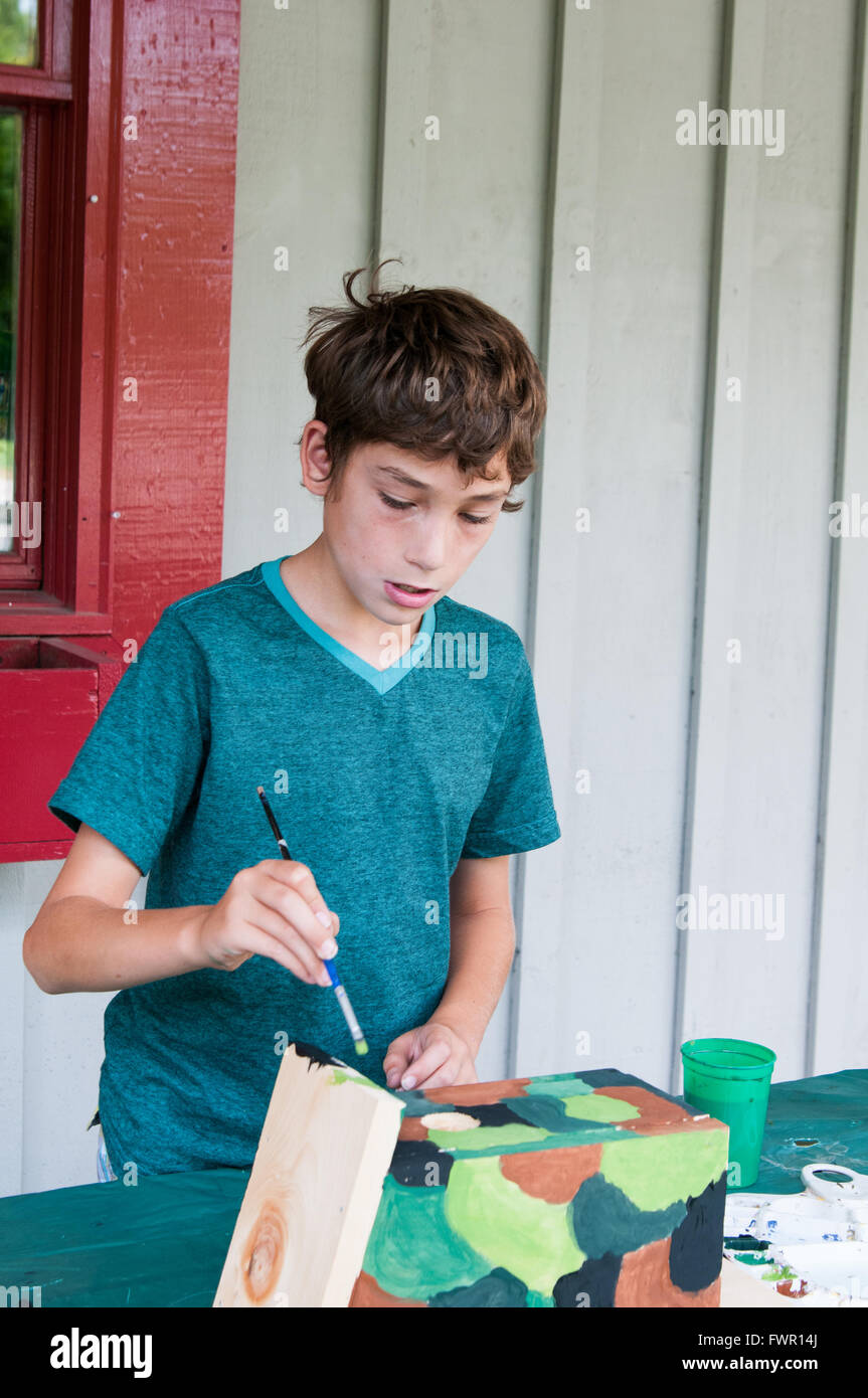 boy at camp painting a birdhouse craft project Stock Photo