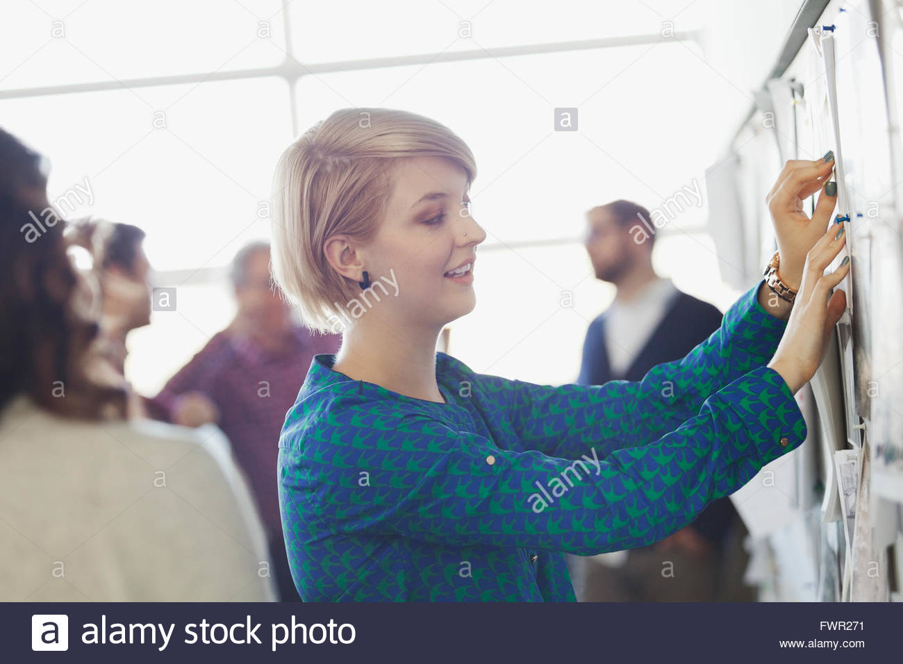 Businesswoman pinning notes on bulletin board Stock Photo