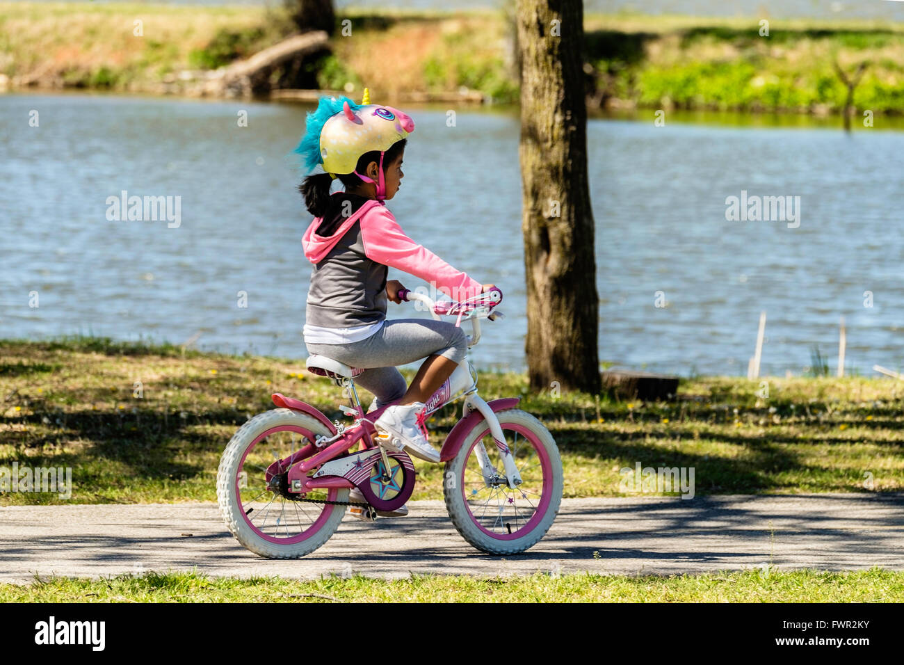 A young Hispanic girl with a unicorn helmet rides her bicycle on the trails at Overholser lake, Oklahoma City, Oklahoma, USA. Stock Photo