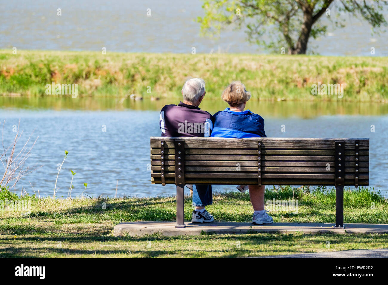 A senior couple sit on a wooden bench in companionship looking out at the North Canadian river and Overholser lake. Oklahoma City, Oklahoma, USA. Stock Photo
