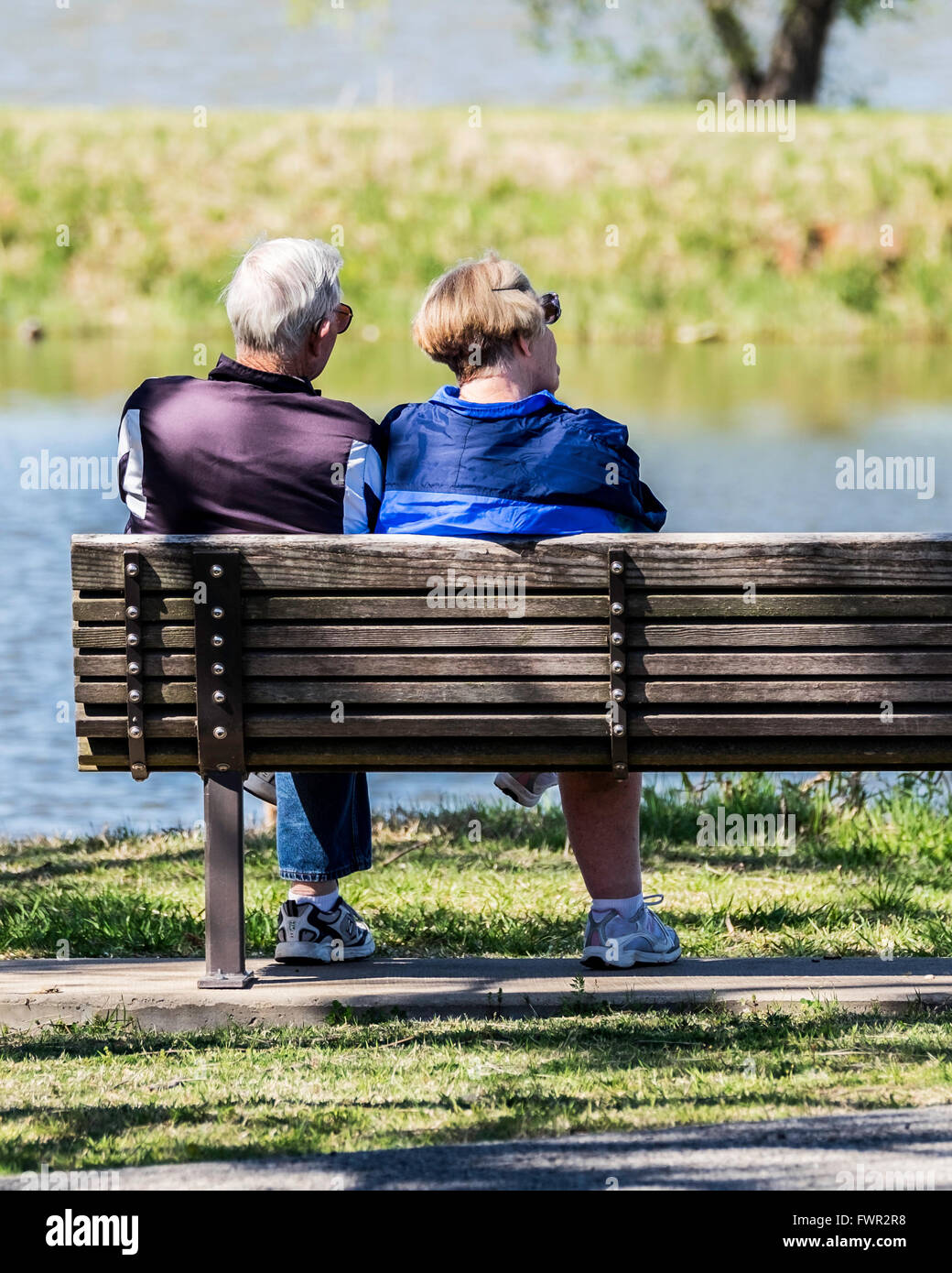 A senior couple sit on a wooden bench in companionship looking out at the North Canadian river and Overholser lake. Oklahoma City, Oklahoma, USA. Stock Photo