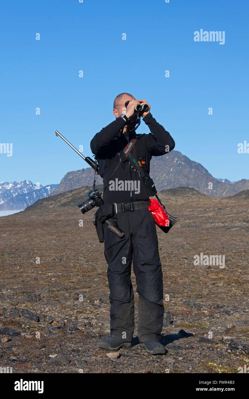 Polar bear guard armed with rifle looking for polar bears through binoculars, Svalbard, Norway Stock Photo