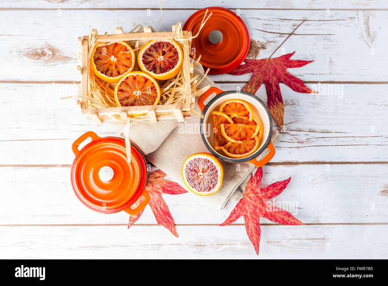 Blood oranges sliced on plates with orange cast iron pots and autumn leaves Stock Photo