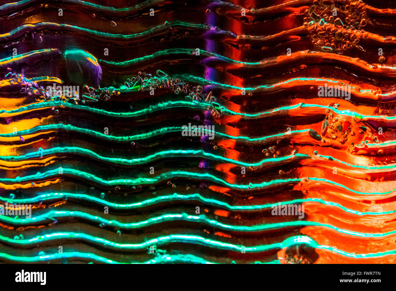 Colored lights behind art glass with waves and air bubbles. Stock Photo