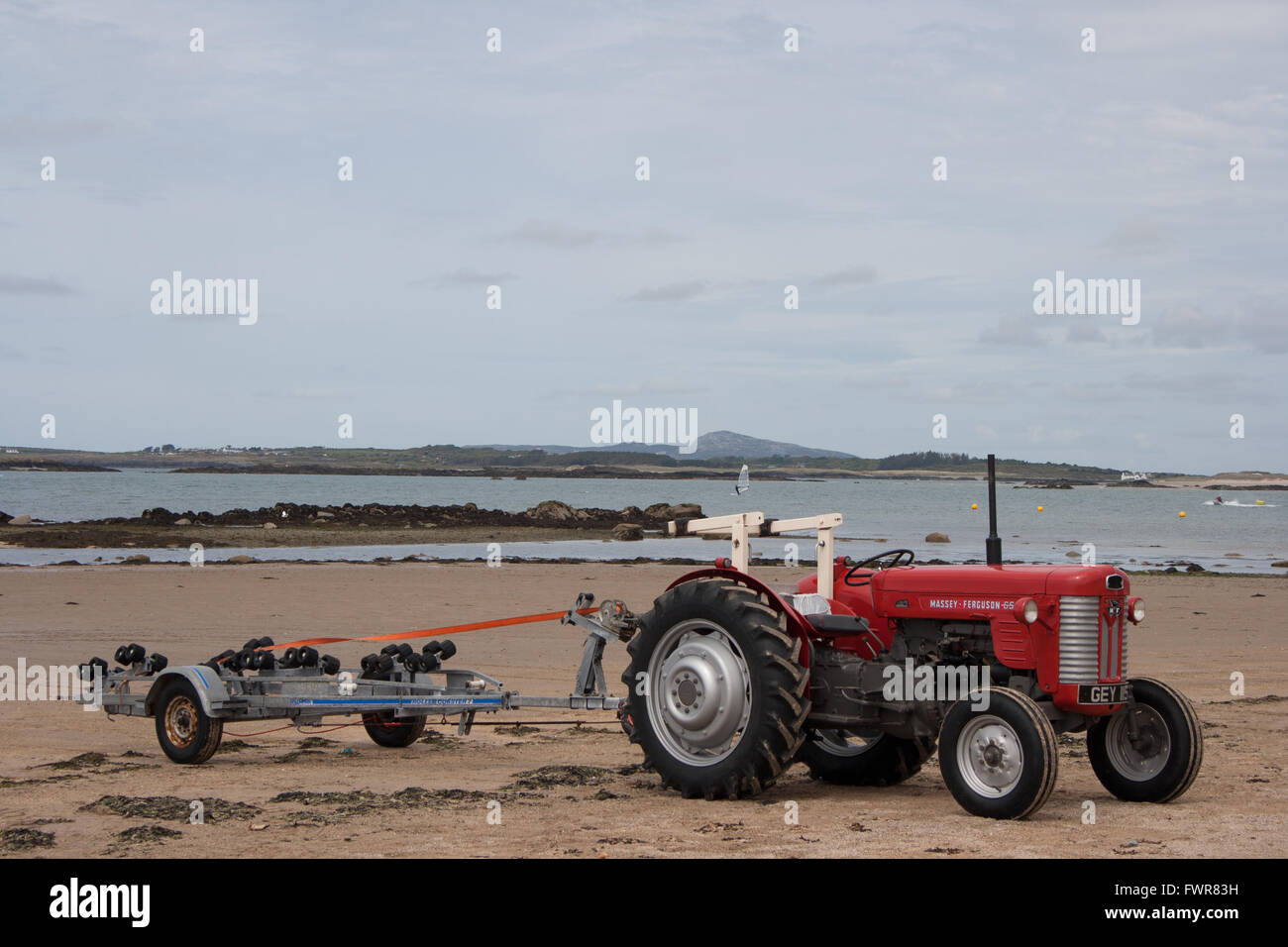 A red Massey Ferguson tractor with empty boat trailer on the beach at Rhosneigr, Anglesey, Wales, UK. Stock Photo