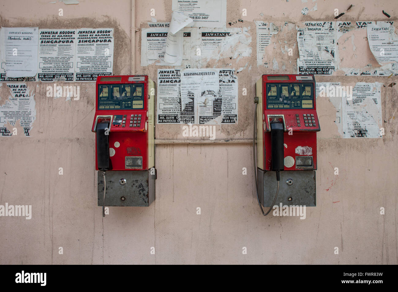 Two old phone boxes or booths hanging on exterior wall. The wall has torn posters and is run down. Stock Photo