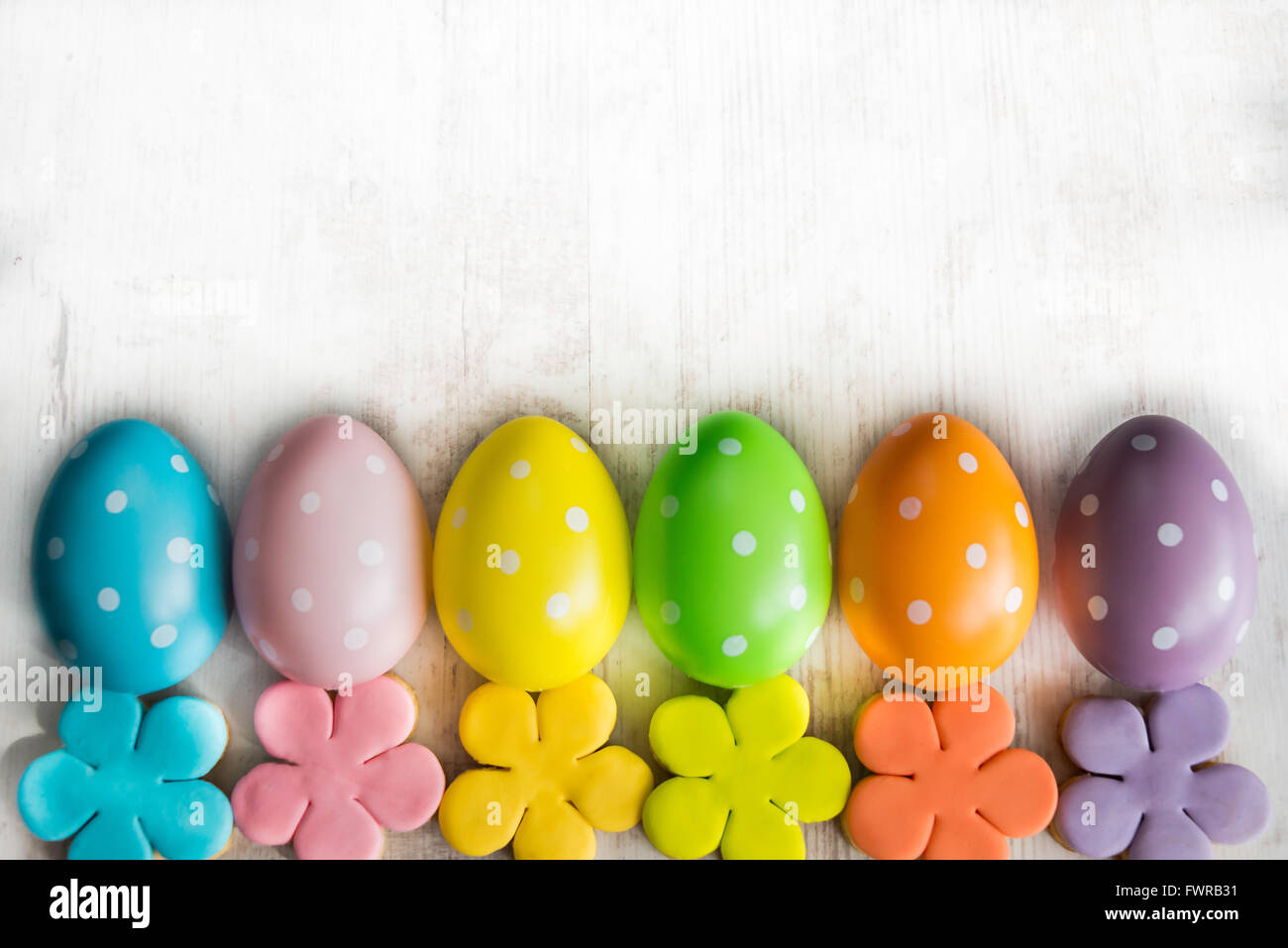 Colorful easter eggs and homemade fondant covered flower cookies on a white wood background Stock Photo