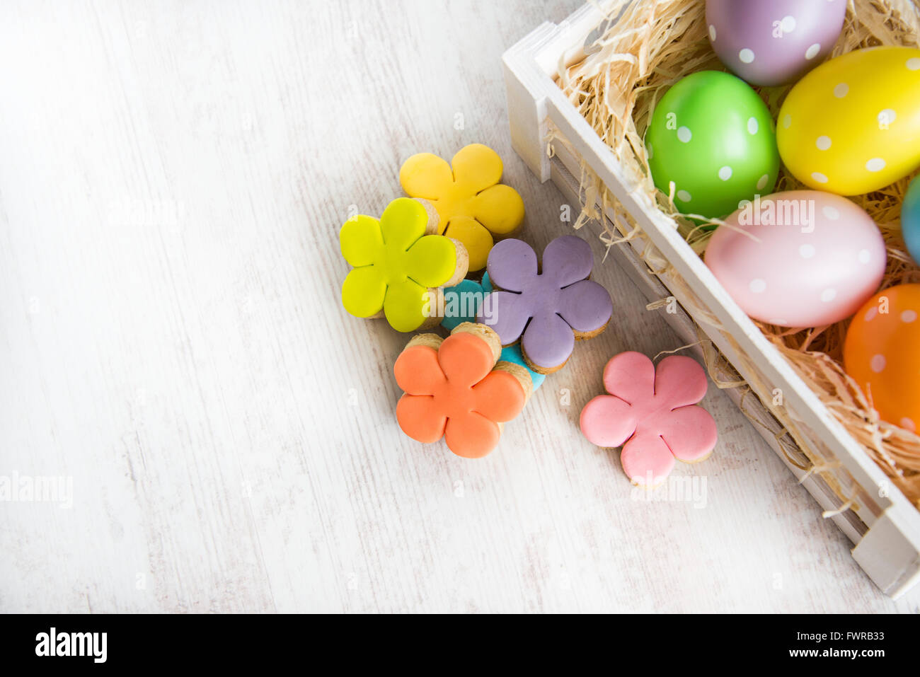 Wooden basket filled with easter eggs and homemade fondant covered flower cut cookies on a white wooden background Stock Photo