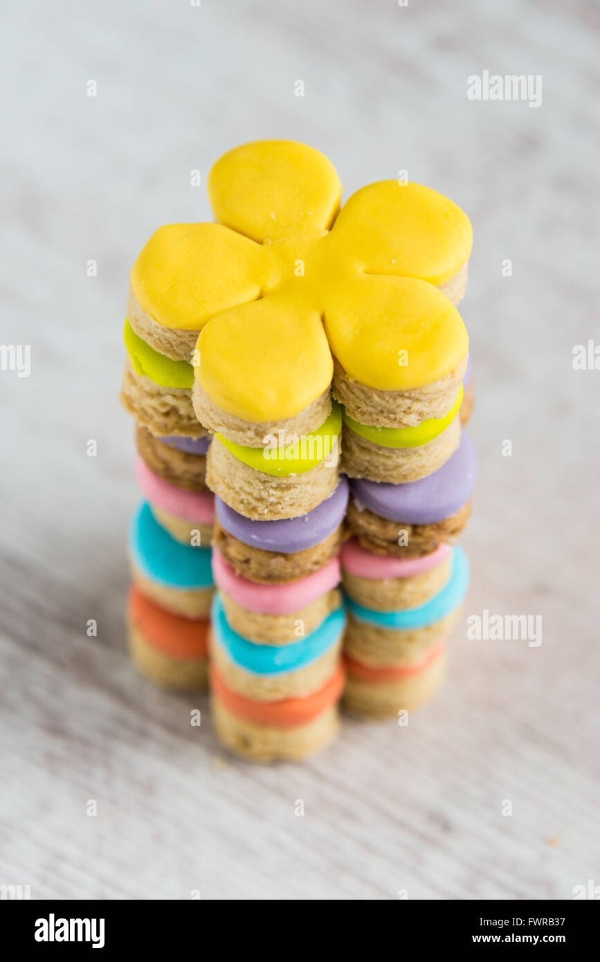 Closeup of colorful flower form homemade fondant covered cookies on a white wooden background Stock Photo
