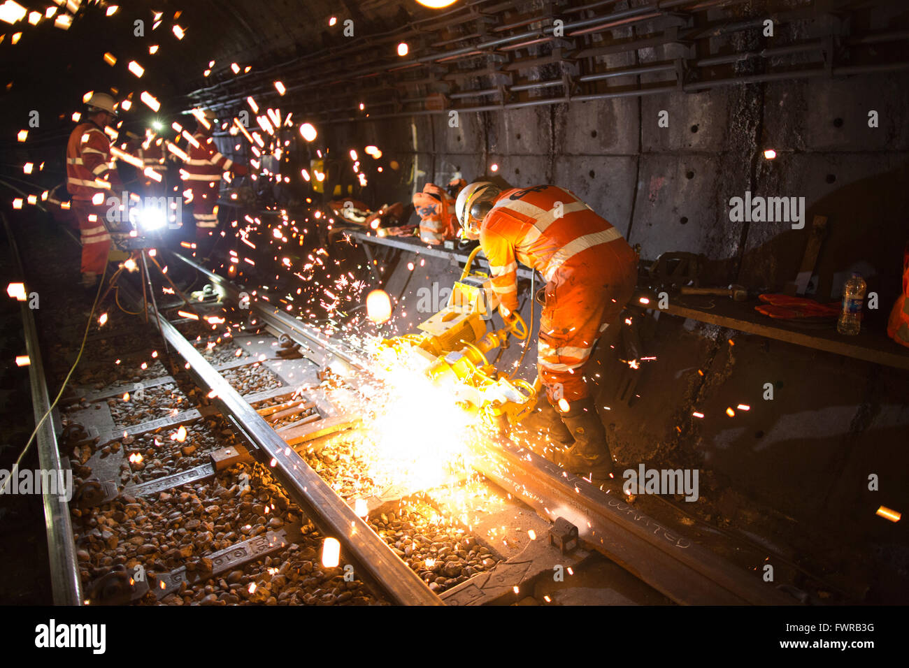 Engineers grinding replacement track components after using thermite welding on London Underground rail track, London, UK Stock Photo
