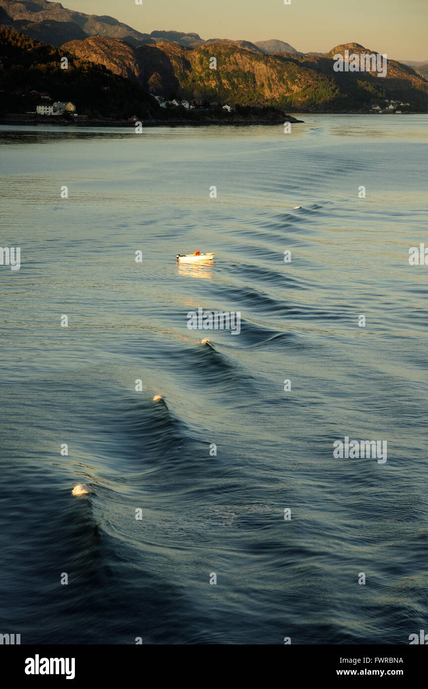 Small boat passing through the wake of a ship sailing through a fjord