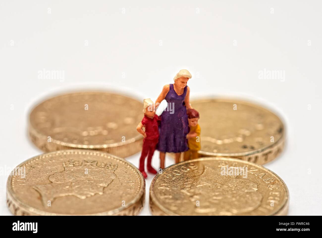 A miniature figurine woman with 2 children standing in between one pound coins Stock Photo
