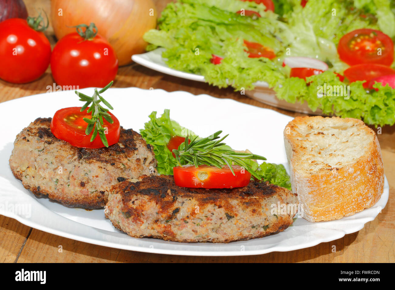 Grilled beef patties, garnished with sliced tomato and rosemary