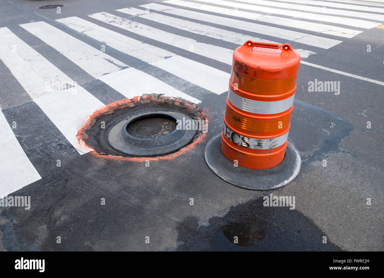 Large traffic drum warns motor vehicles and pedestrians of the danger of a broken sewer entrance Stock Photo