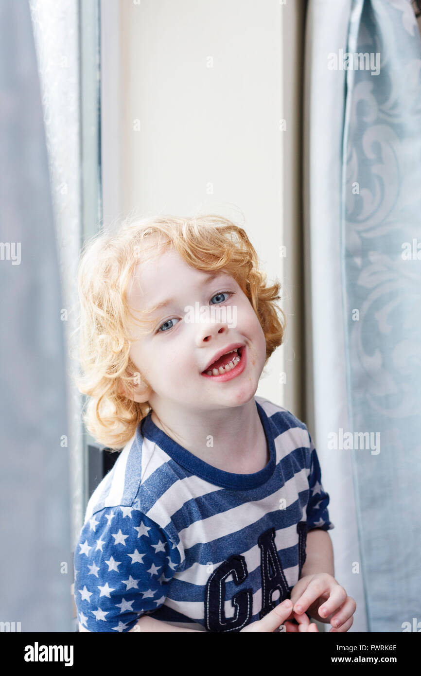 A small caucasion blond haired boy sat by a window, smiling Stock Photo