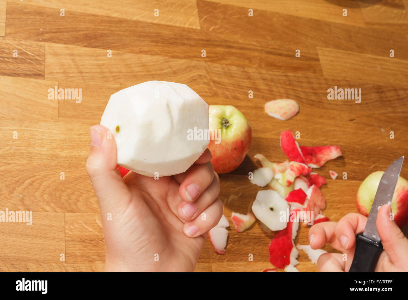 A hand holding a peeled apple over a pile of peelings Stock Photo