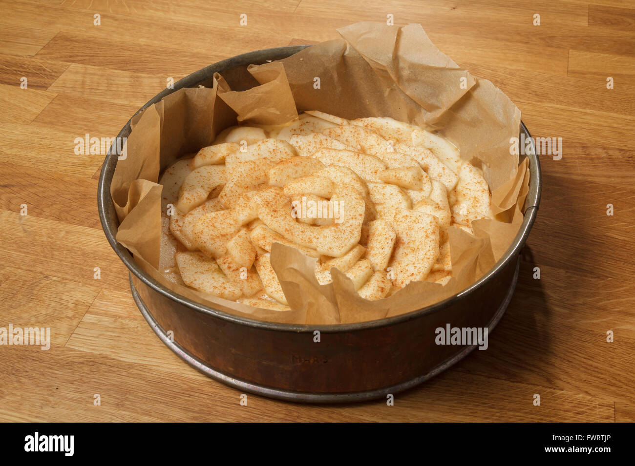 Unbaked apple pie in a metal springform standing on a wooden table, with apple slices and cinnamon on top Stock Photo