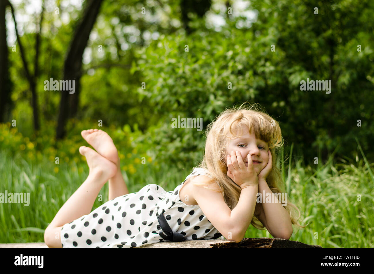 beautiful blond girl lying on wooden bench in forrest Stock Photo