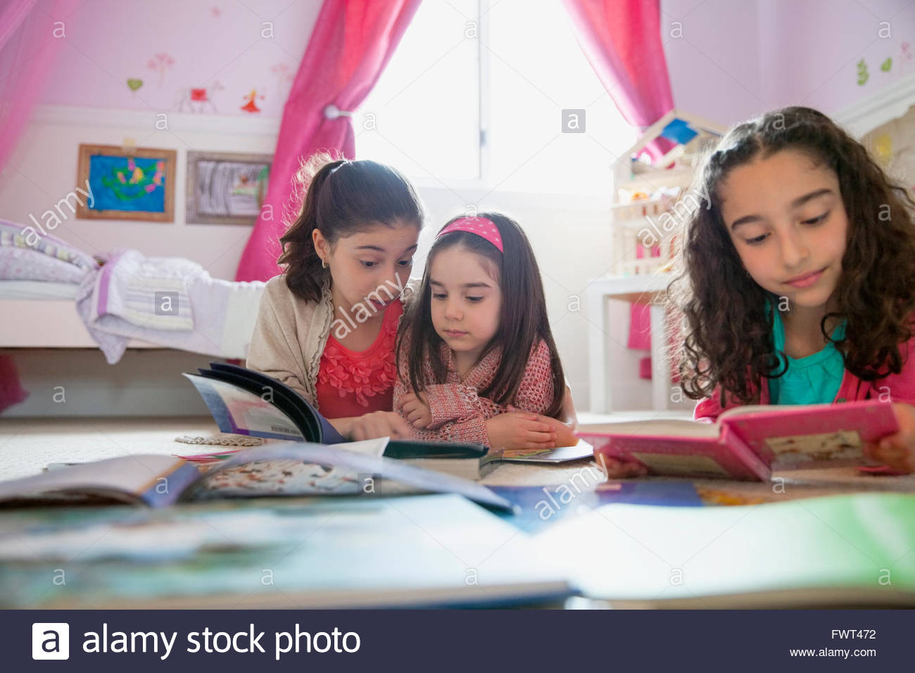Little sisters reading while lying on floor Stock Photo