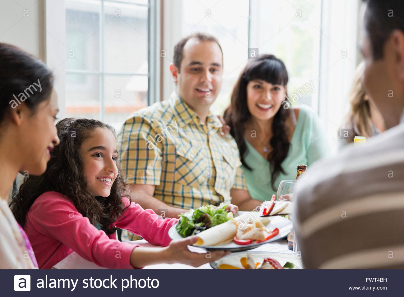 Little girl passing plate to man at dining table Stock Photo