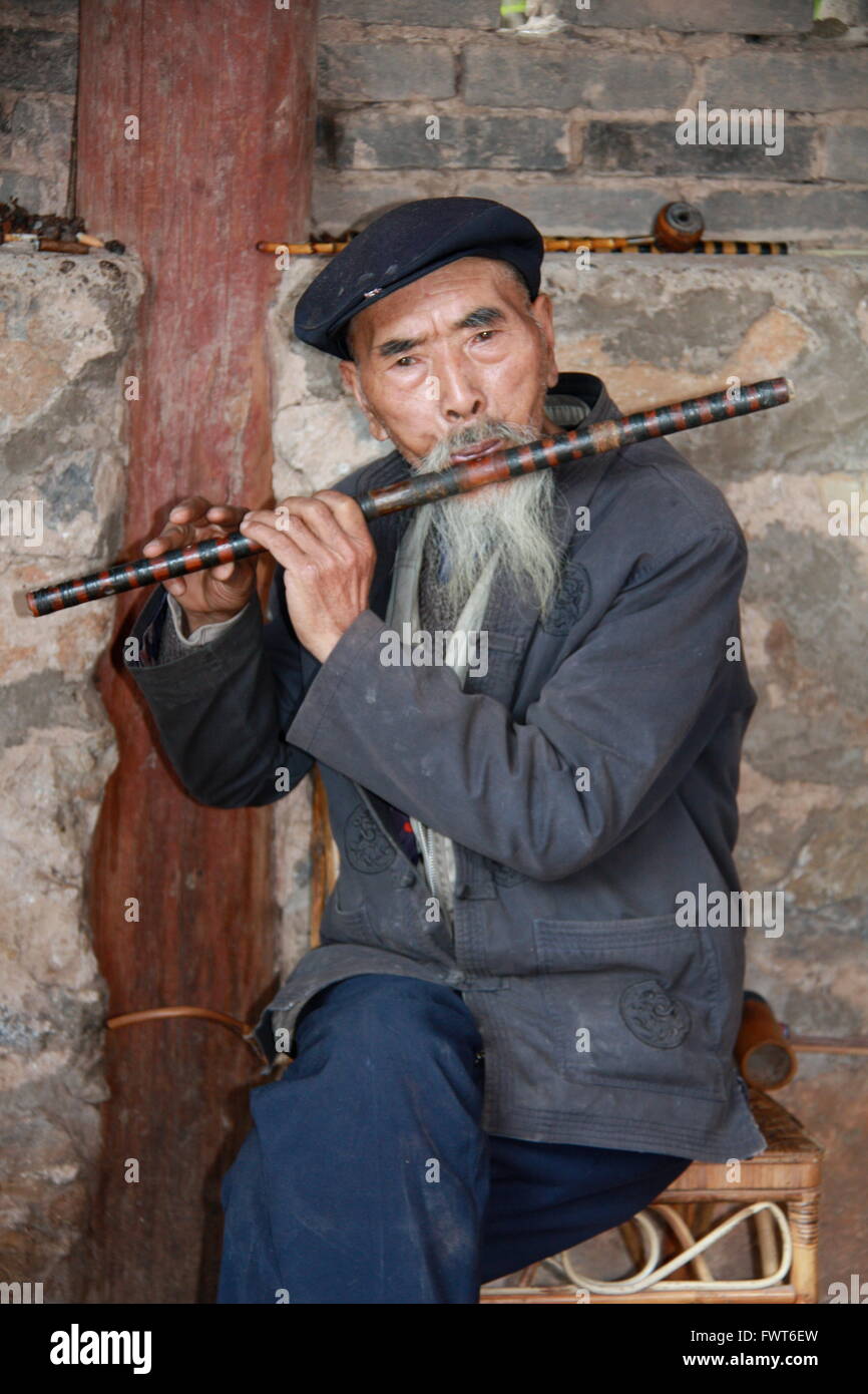 Elderly Chinese man playing a dizi, a Chinese flute in Shigu, near the