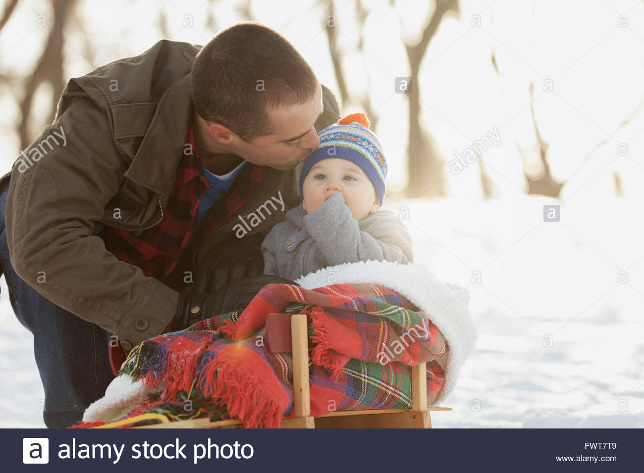 Father kissing baby boy sitting on toboggan Stock Photo Alamy