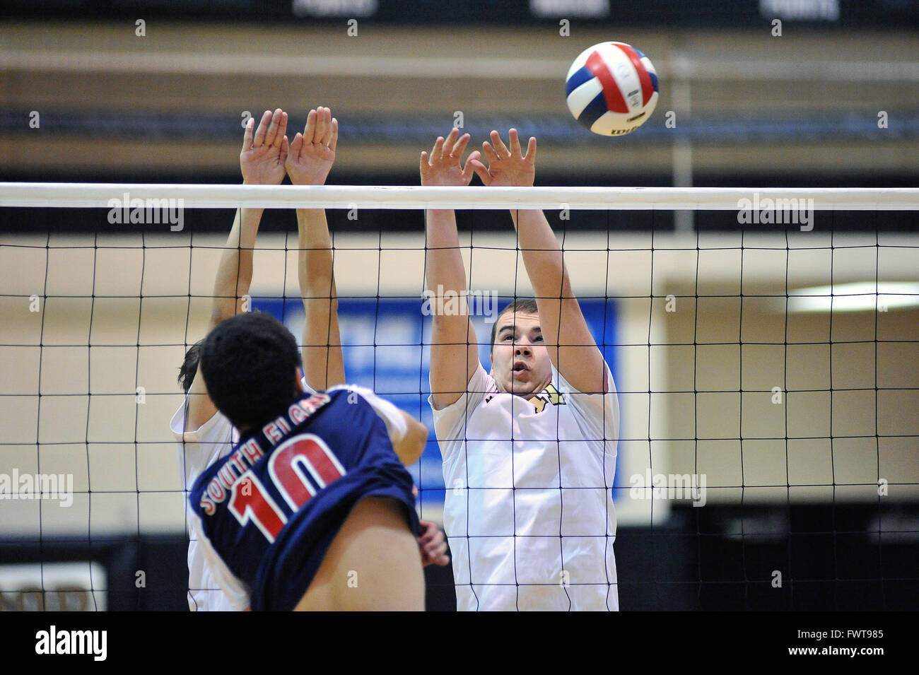 Players rise in an attempt to block a kill shot during a high school volleyball match. USA. Stock Photo