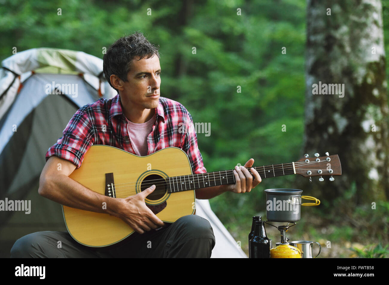 Caucasian man playing guitar at a camp site Stock Photo