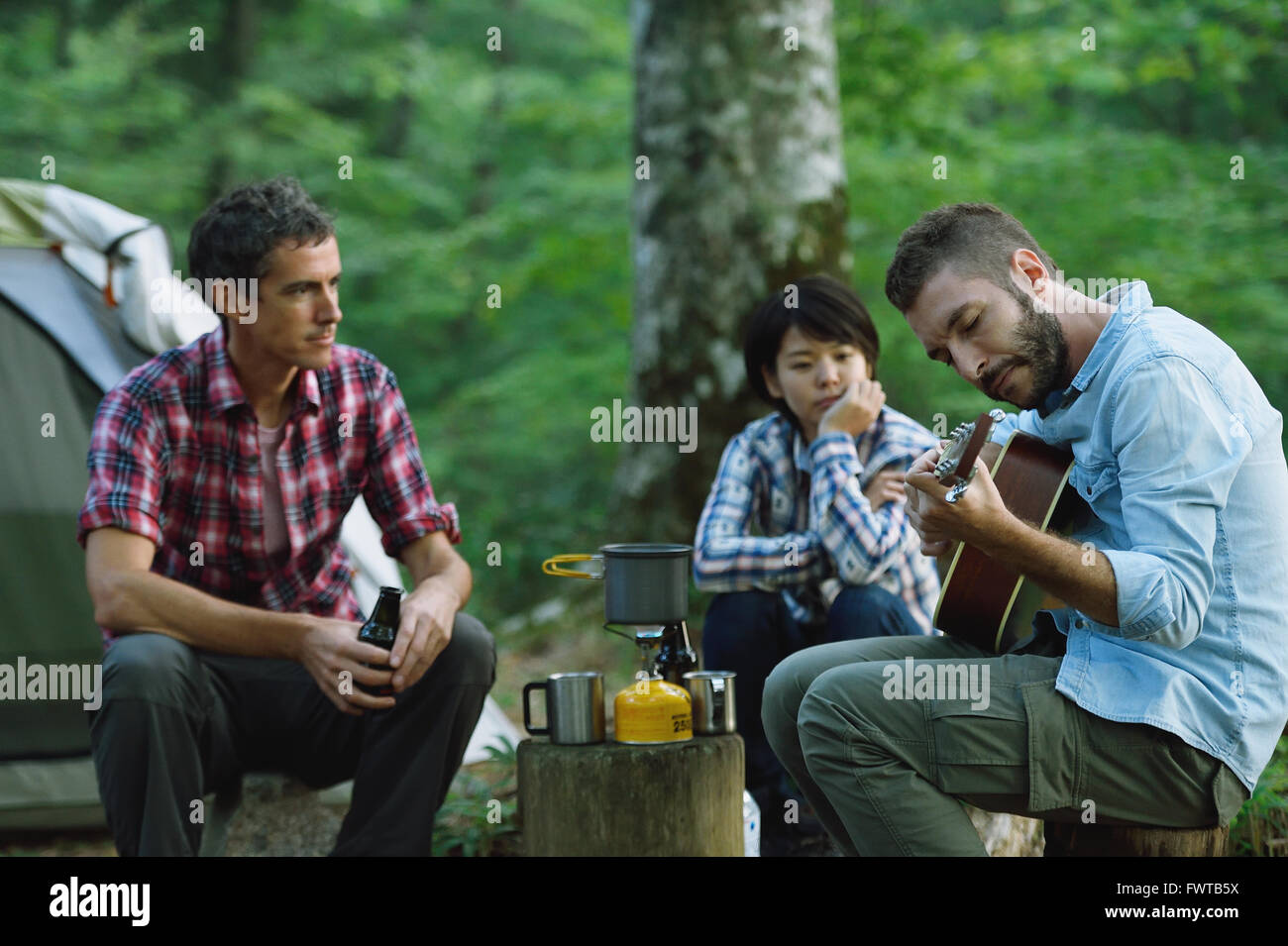 Multi-ethnic group of friends playing guitar at a camp site Stock Photo