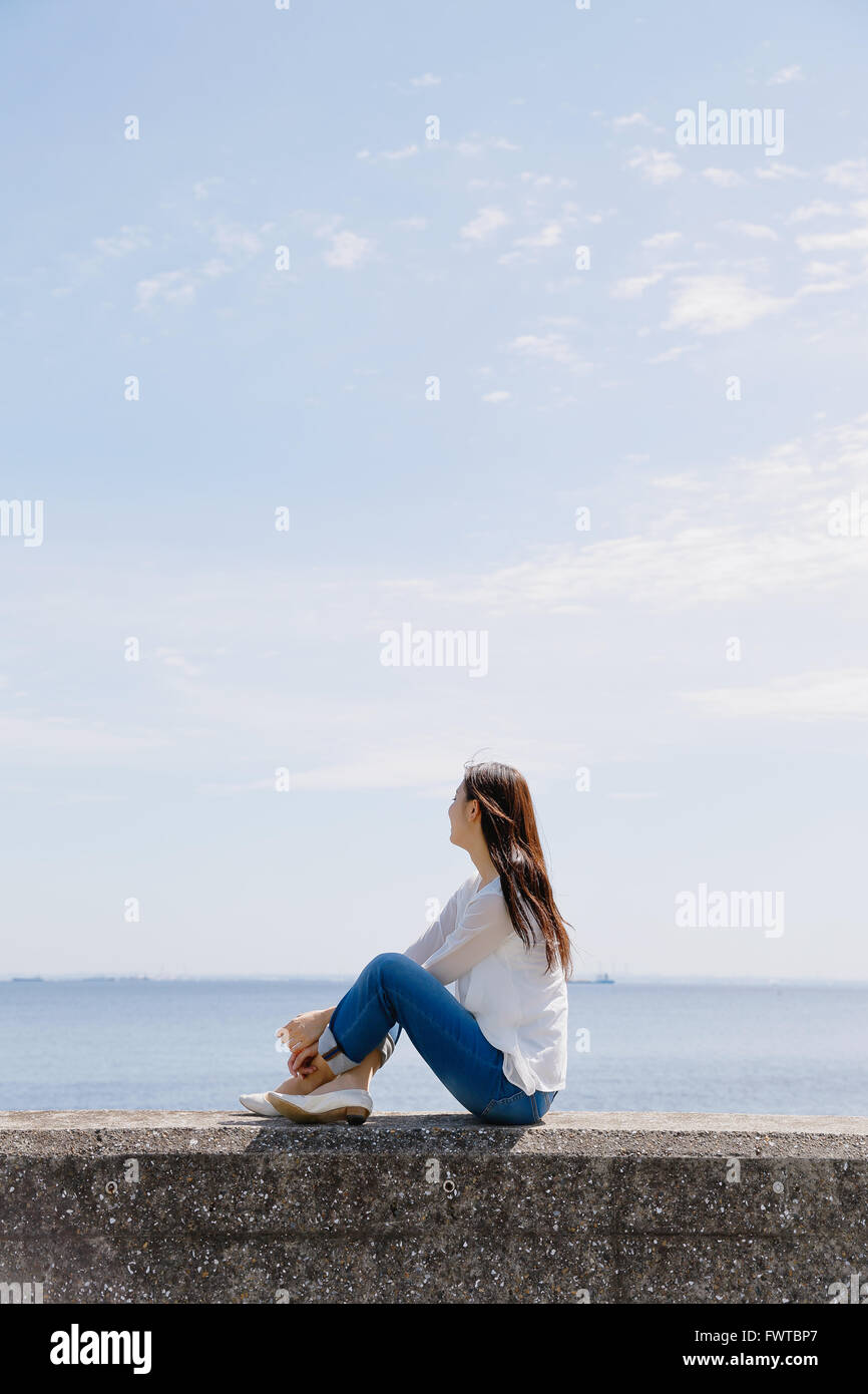 Young Japanese woman sitting on concrete wall by the sea Stock Photo ...