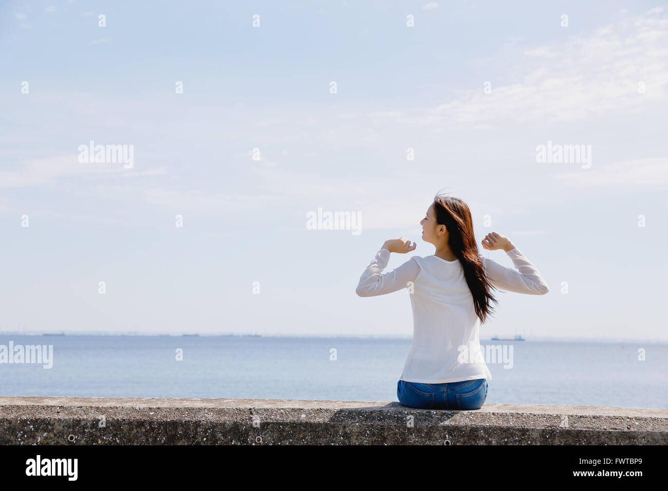 Young Japanese woman sitting on concrete wall by the sea Stock Photo ...