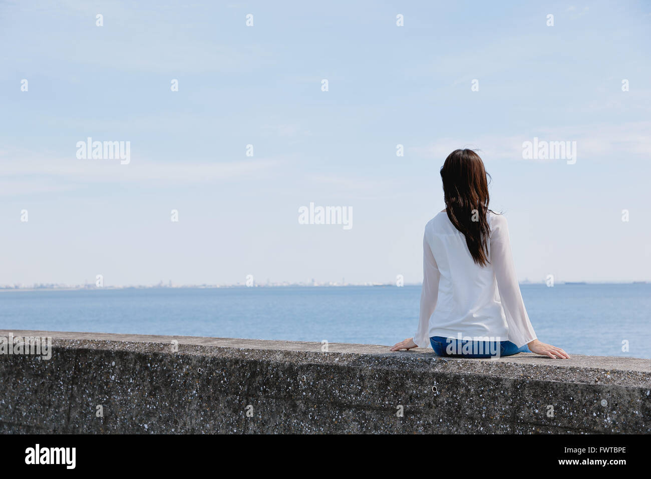 Young Japanese woman sitting on concrete wall by the sea Stock Photo ...