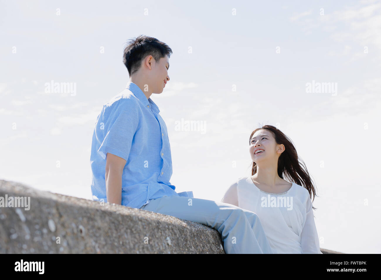 Young Japanese couple sitting on concrete wall by the sea Stock Photo ...