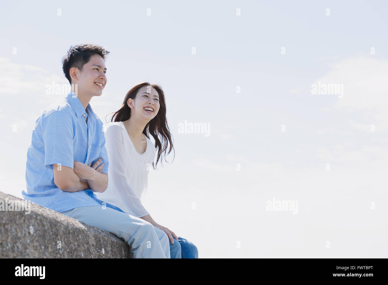 Young Japanese couple sitting on concrete wall by the sea Stock Photo ...