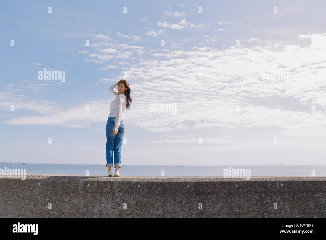 Young Japanese woman standing on concrete wall by the sea Stock Photo ...