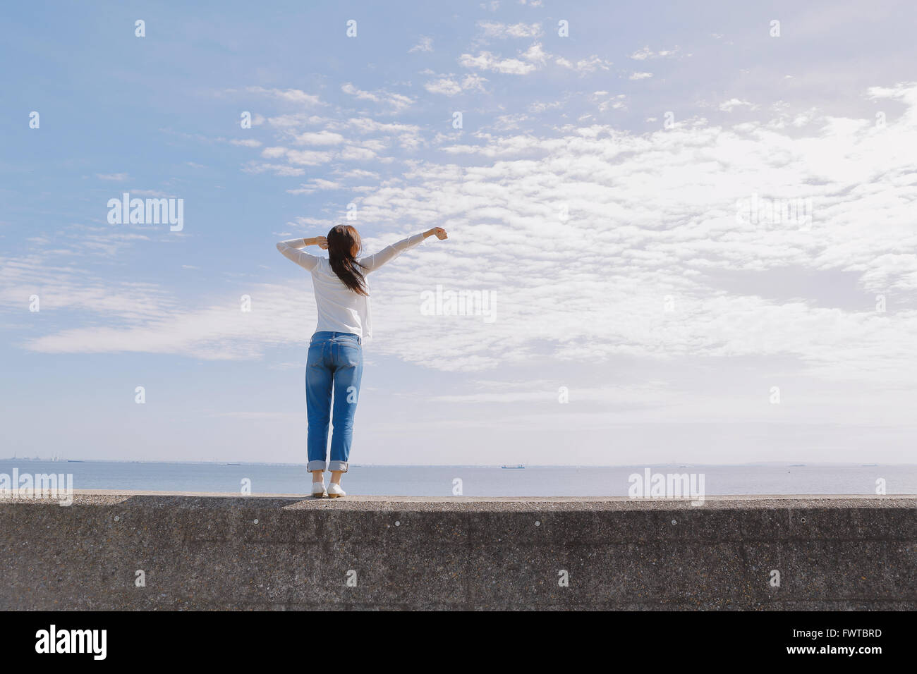 Young Japanese woman standing on concrete wall by the sea Stock Photo ...