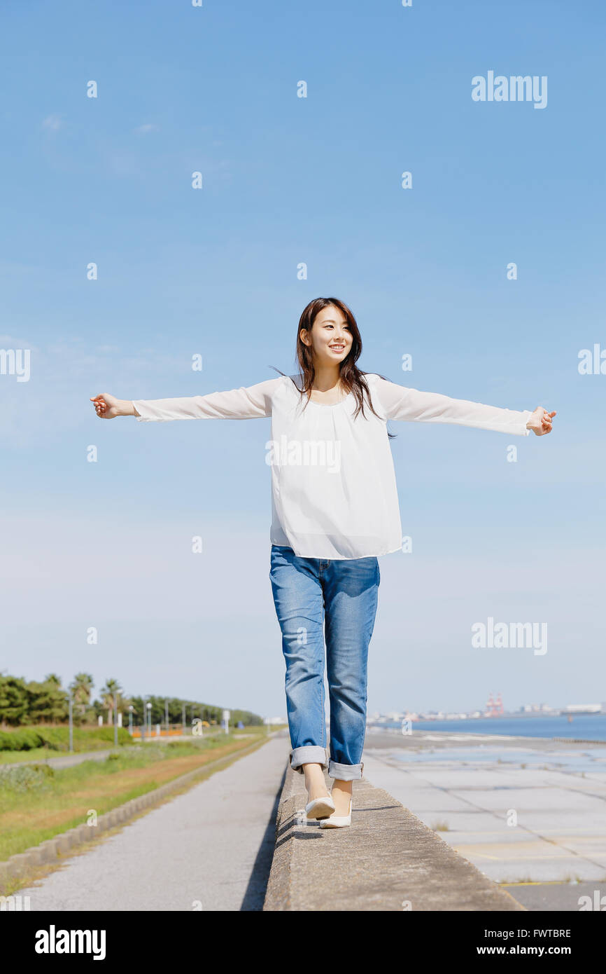 Young Japanese woman standing on concrete wall by the sea Stock Photo ...