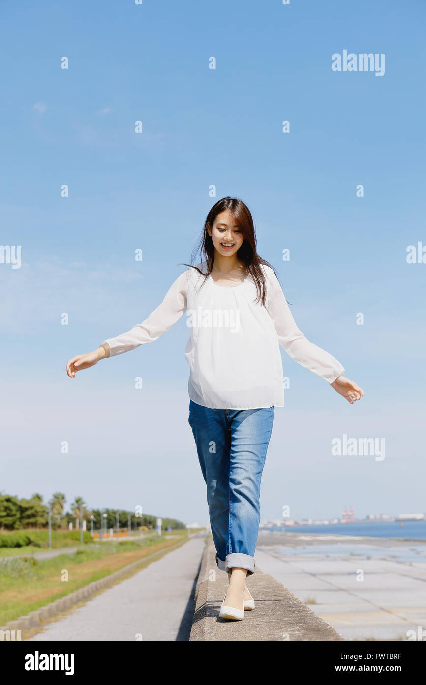 Young Japanese woman standing on concrete wall by the sea Stock Photo ...