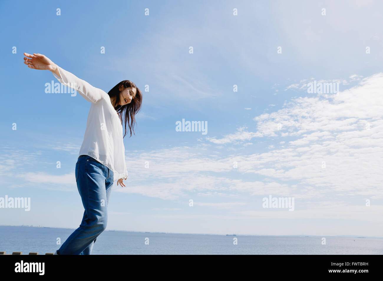 Young Japanese woman standing on concrete wall by the sea Stock Photo ...