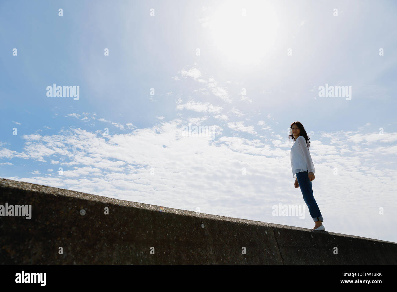 Young Japanese woman standing on concrete wall by the sea Stock Photo ...