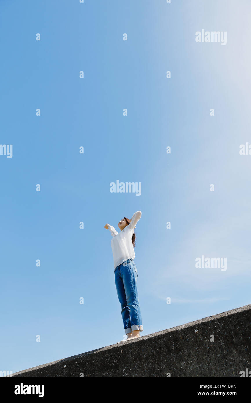 Young Japanese woman standing on concrete wall by the sea Stock Photo ...