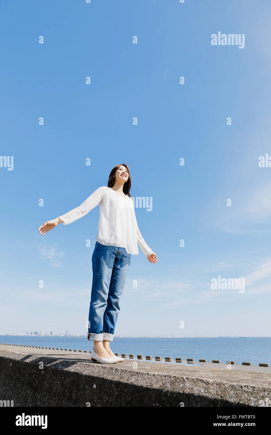 Young Japanese woman standing on concrete wall by the sea Stock Photo ...
