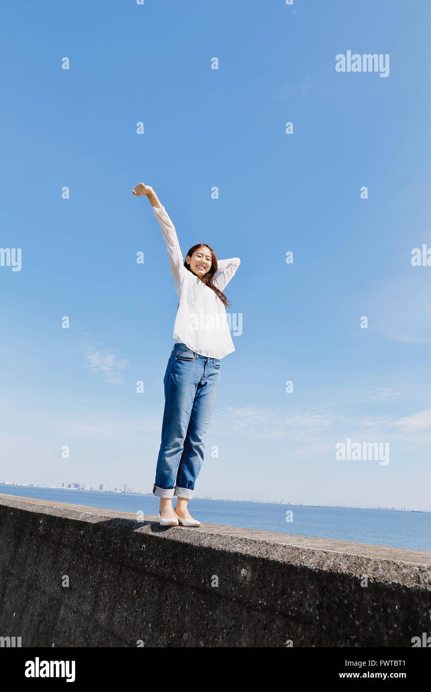 Young Japanese woman standing on concrete wall by the sea Stock Photo ...