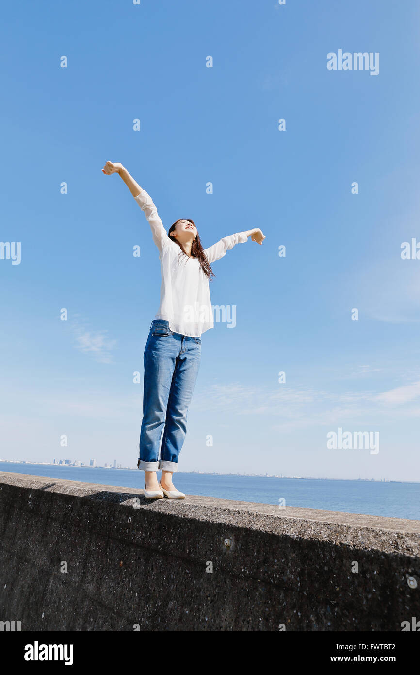 Young Japanese woman standing on concrete wall by the sea Stock Photo ...