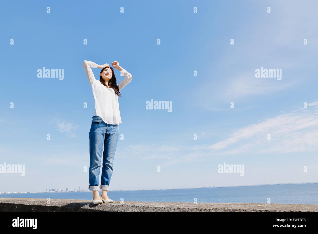 Young Japanese woman standing on concrete wall by the sea Stock Photo ...