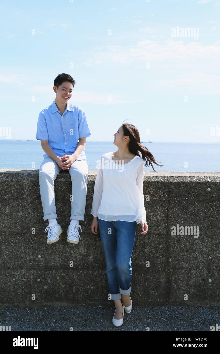Young Japanese couple sitting on concrete wall by the sea Stock Photo ...