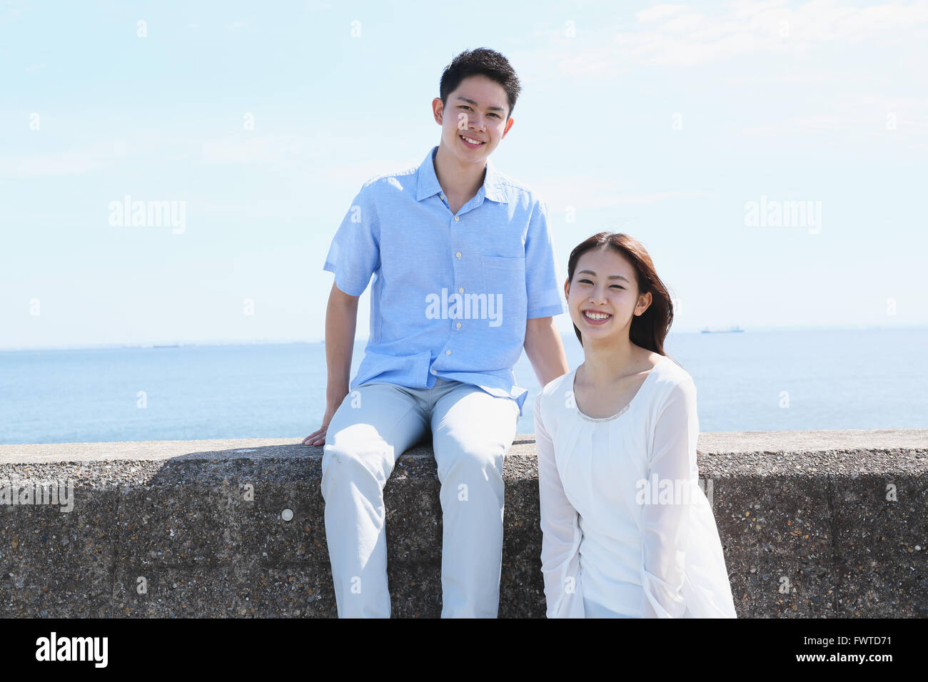 Young Japanese couple sitting on concrete wall by the sea Stock Photo ...