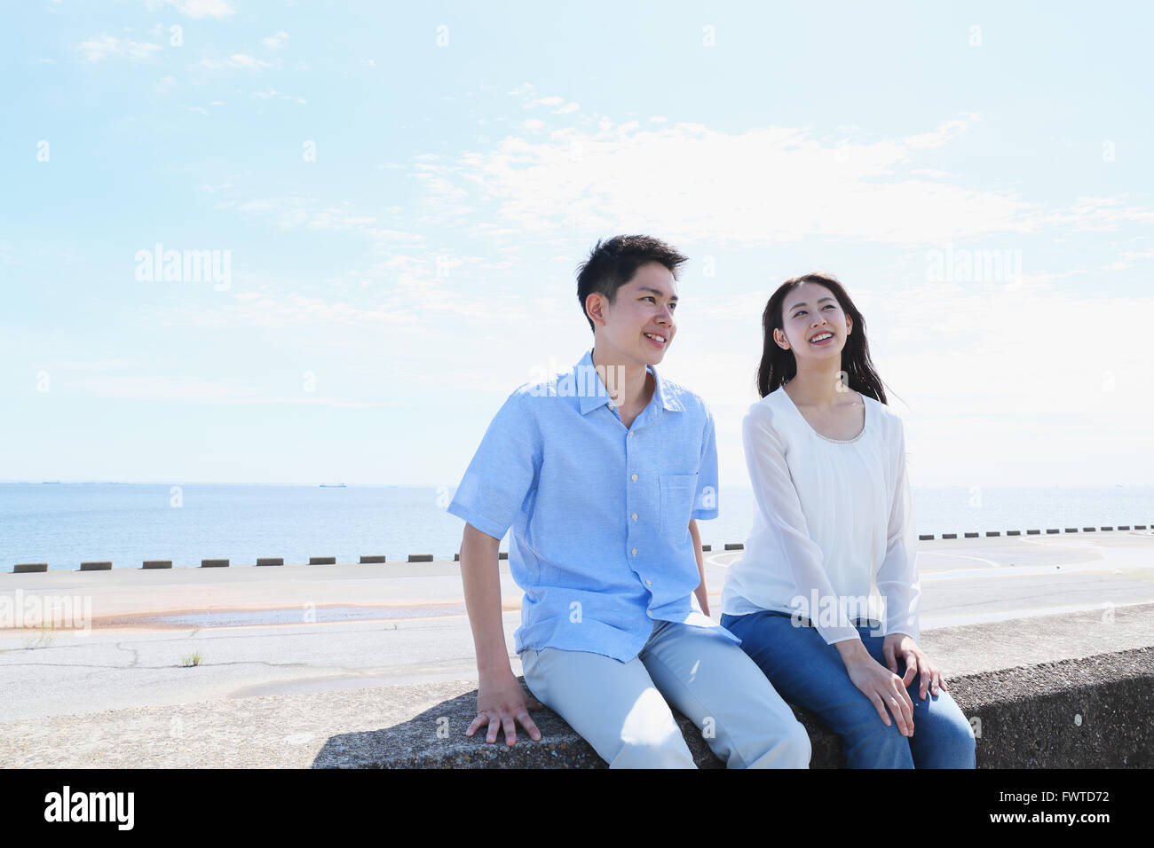 Young Japanese couple sitting on concrete wall by the sea Stock Photo ...